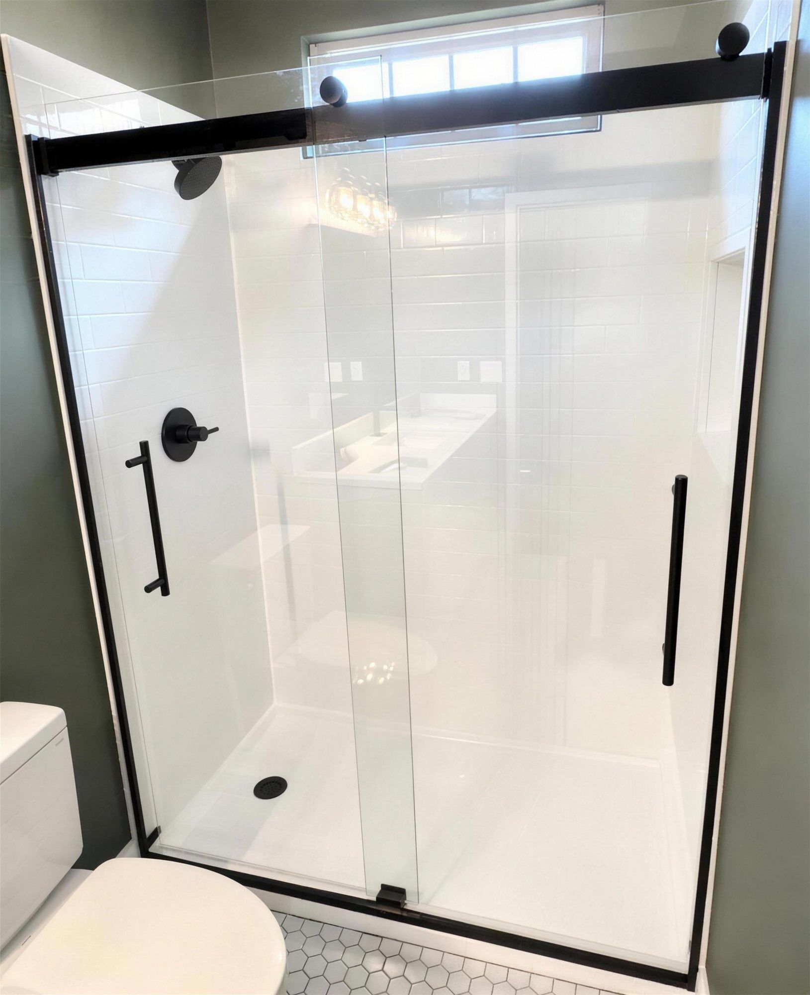 St. Louis bathroom remodel with a white tile walk-in shower, black frameless sliding glass door, black fixtures, and a penny-and-hex tile floor